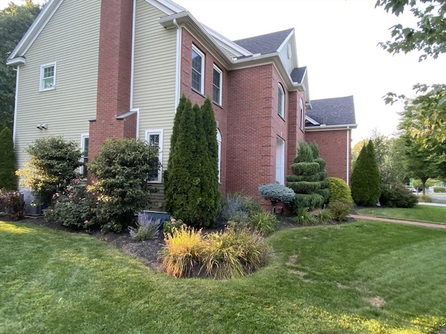 view of side of property with brick siding, a lawn, and a chimney