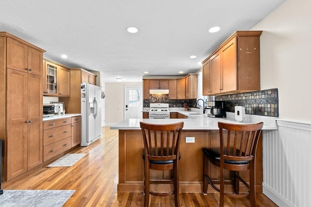 kitchen with kitchen peninsula, a breakfast bar, white appliances, and light wood-type flooring