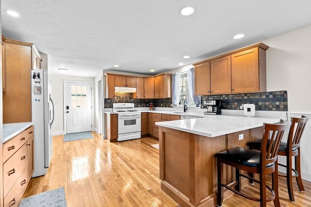 kitchen featuring white appliances, a kitchen breakfast bar, sink, light wood-type flooring, and kitchen peninsula