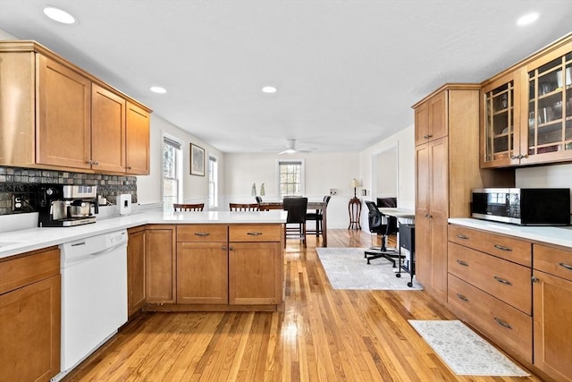 kitchen with ceiling fan, light hardwood / wood-style flooring, kitchen peninsula, white dishwasher, and decorative backsplash