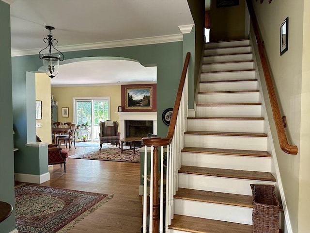 stairway with crown molding, baseboards, a fireplace, wood finished floors, and arched walkways