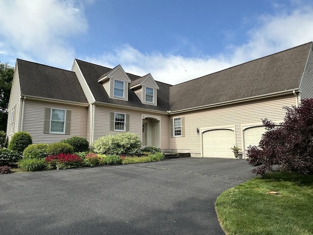 cape cod home featuring driveway, a shingled roof, and a garage