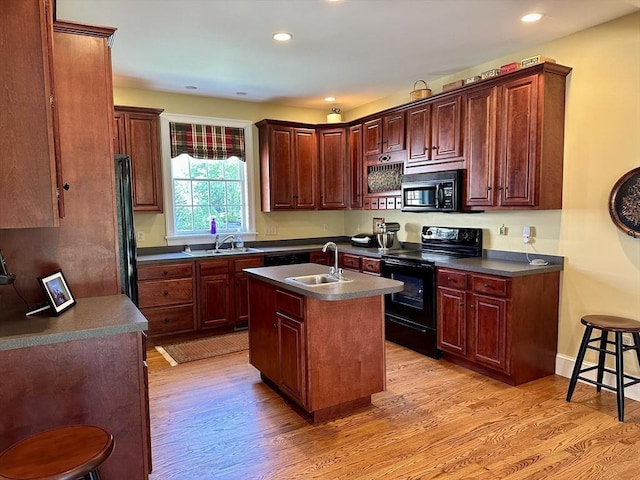 kitchen with black appliances, an island with sink, light wood finished floors, and a sink