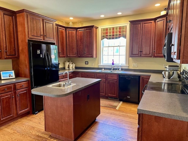 kitchen with a center island with sink, light wood-style flooring, black appliances, and a sink