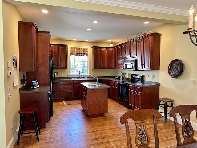 kitchen featuring dark countertops, baseboards, light wood-style floors, black appliances, and a kitchen island with sink