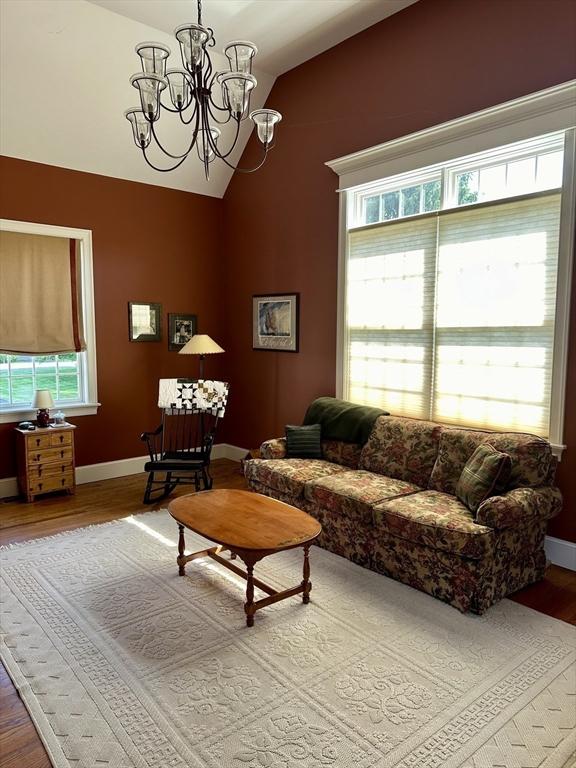 living room with plenty of natural light, an inviting chandelier, lofted ceiling, and wood finished floors