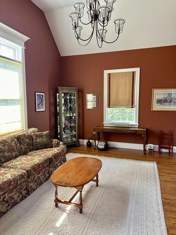 living area featuring vaulted ceiling, a notable chandelier, wood finished floors, and a healthy amount of sunlight