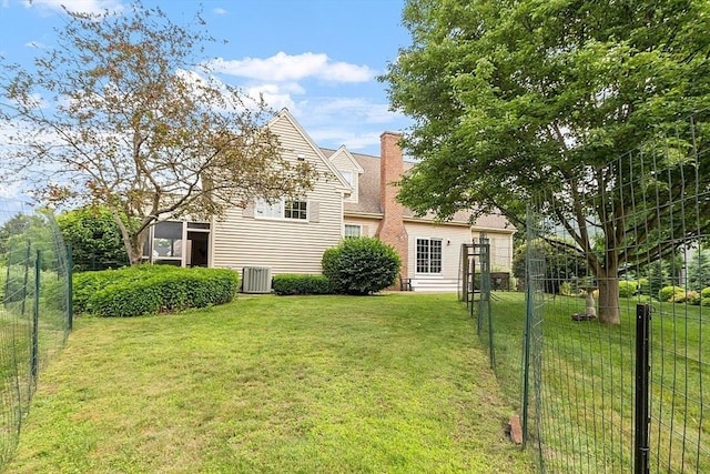 rear view of house with a yard, central air condition unit, a chimney, and fence