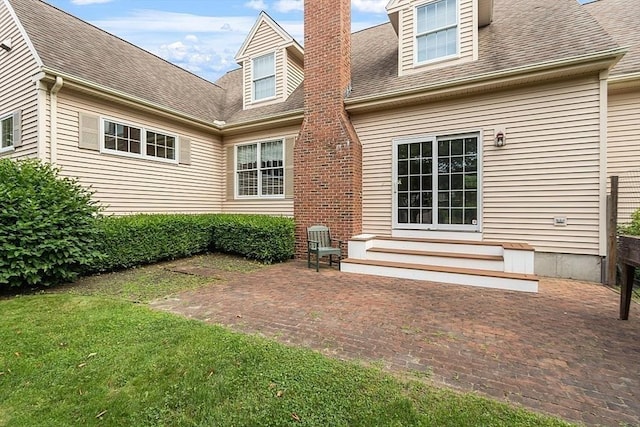 rear view of property featuring entry steps, a chimney, a patio, and roof with shingles