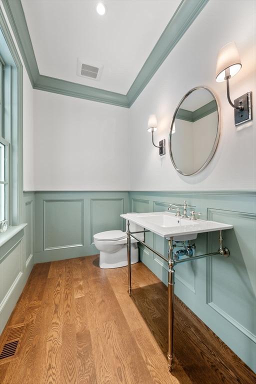 61 Heath St, Brookline, MA 02445 - bathroom featuring a decorative wall, wood finished floors, toilet, a wainscoted wall, and crown molding