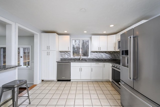 kitchen with sink, stainless steel appliances, tasteful backsplash, dark stone counters, and white cabinets