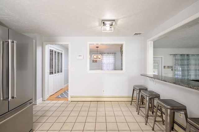 interior space with stone counters, baseboard heating, pendant lighting, high quality fridge, and light tile patterned floors