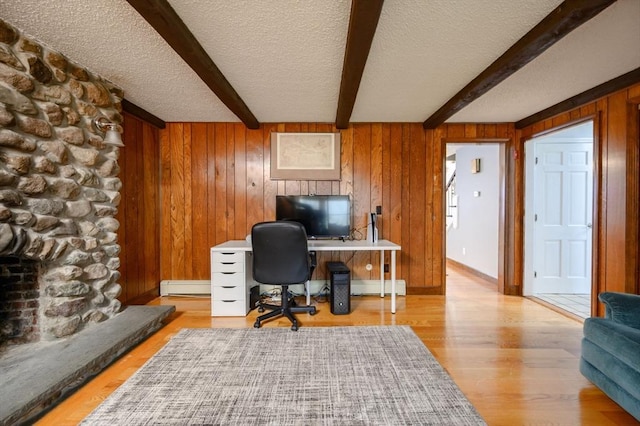 office space with baseboard heating, beamed ceiling, a textured ceiling, wooden walls, and a fireplace