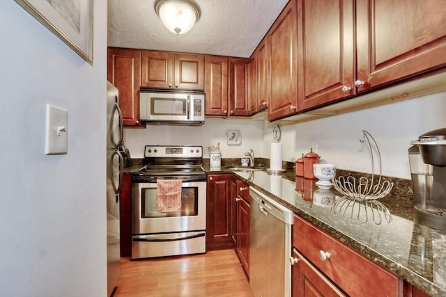 kitchen featuring dark stone countertops, sink, stainless steel appliances, and light hardwood / wood-style floors