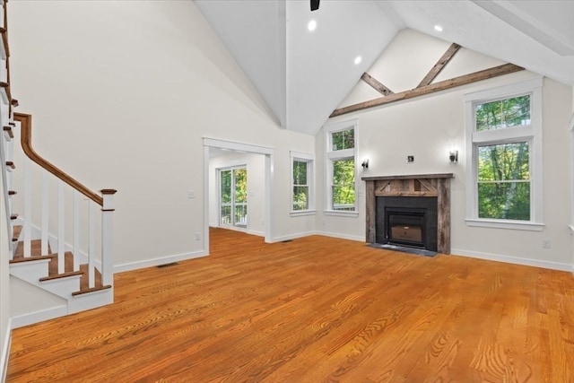 unfurnished living room featuring light wood-type flooring, high vaulted ceiling, and beamed ceiling