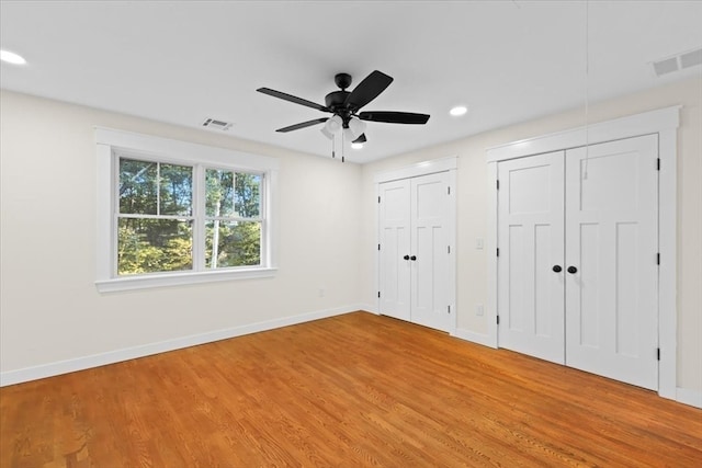 unfurnished bedroom with ceiling fan, light wood-type flooring, and two closets