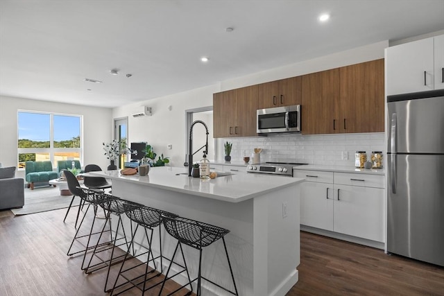 kitchen with a sink, stainless steel appliances, light countertops, a kitchen bar, and backsplash