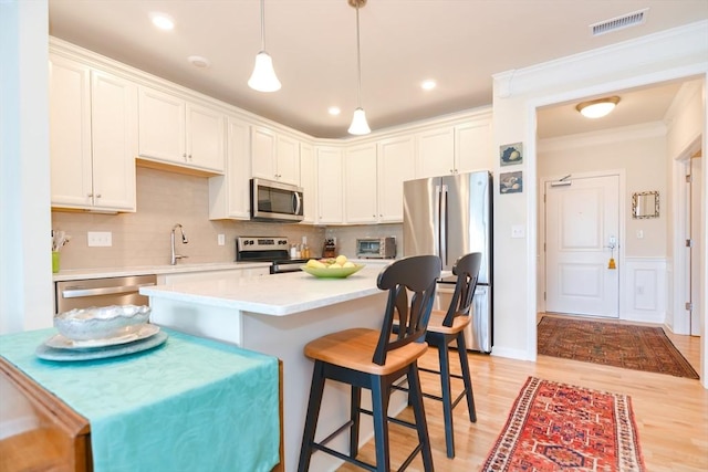 kitchen featuring a kitchen bar, visible vents, stainless steel appliances, white cabinets, and light countertops