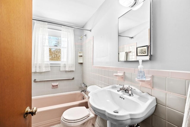 full bathroom featuring tiled shower / bath combo, sink, tile walls, and toilet