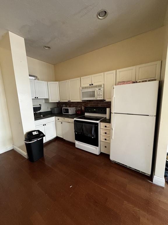 kitchen with dark wood-style flooring, dark countertops, white cabinets, white appliances, and baseboards