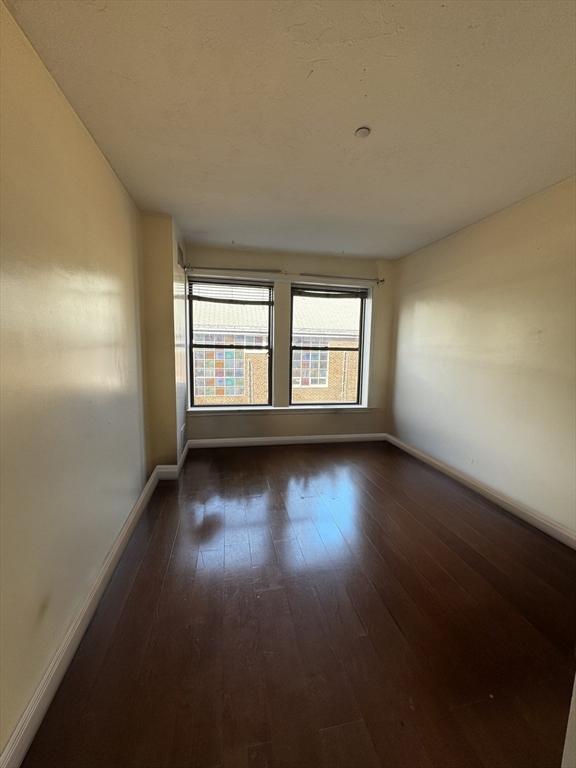 empty room with dark wood-type flooring and baseboards