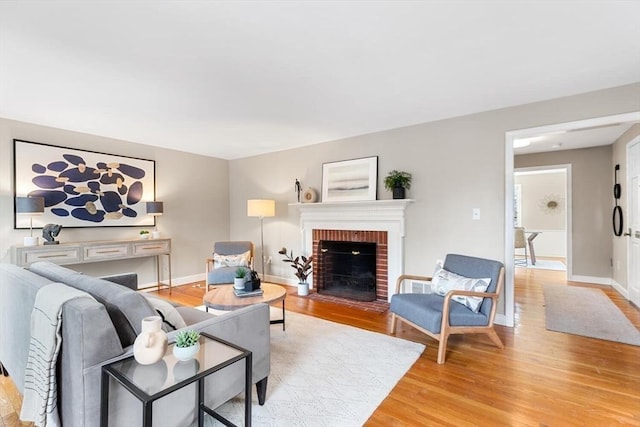 living room featuring baseboards, a brick fireplace, and light wood-style floors