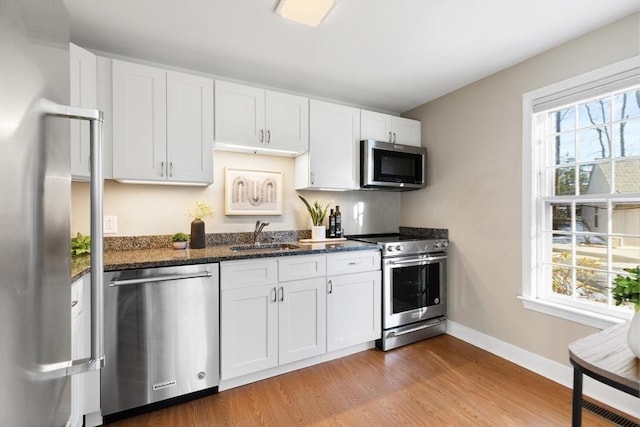 kitchen with light wood finished floors, appliances with stainless steel finishes, white cabinetry, a sink, and baseboards