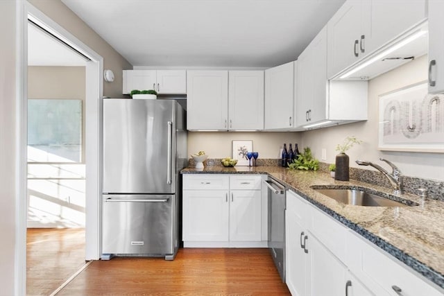 kitchen featuring light wood finished floors, appliances with stainless steel finishes, stone counters, white cabinetry, and a sink