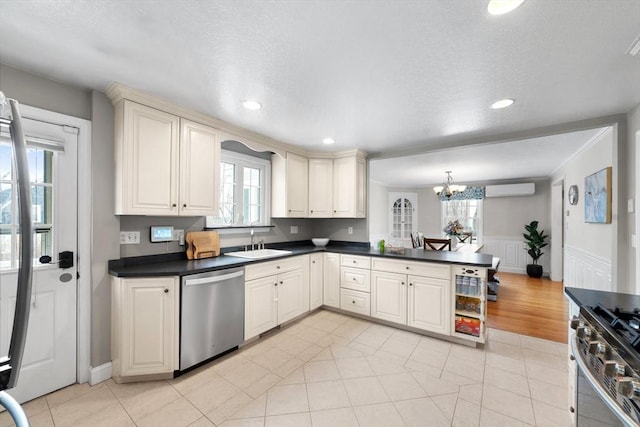 kitchen featuring stainless steel appliances, a peninsula, a sink, an AC wall unit, and dark countertops