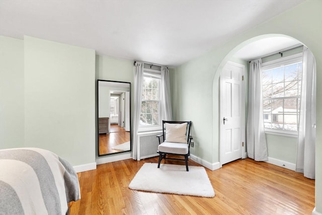 living area with light wood-style flooring, baseboards, and arched walkways