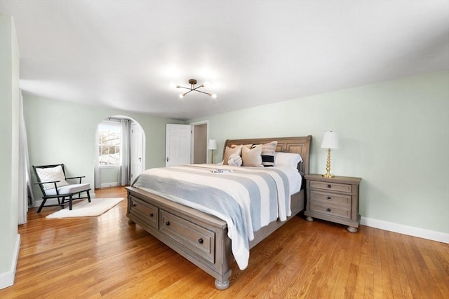 bedroom featuring arched walkways, light wood-style flooring, and baseboards