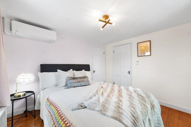 bedroom featuring baseboards, wood finished floors, and a wall mounted air conditioner