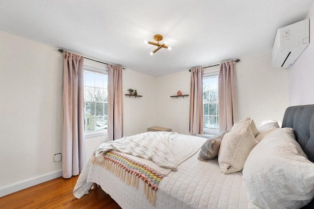 bedroom featuring wood finished floors, multiple windows, baseboards, and a wall mounted AC