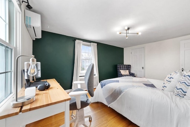 bedroom with an accent wall, a wall mounted air conditioner, and wood finished floors