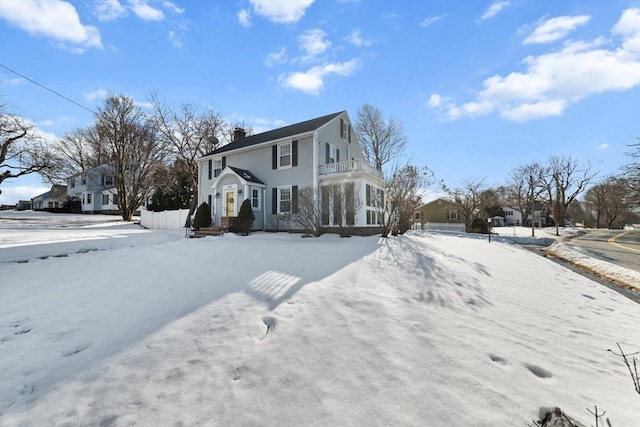 view of snow covered exterior with a residential view, a chimney, and a balcony