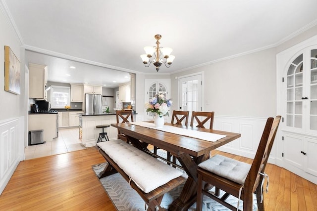 dining area featuring a notable chandelier, a decorative wall, light wood-style flooring, ornamental molding, and wainscoting