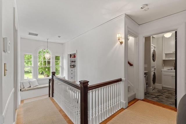 59 Elm St, Concord, MA 01742 - hall with stacked washing machine and dryer, light wood-style flooring, a sink, and an upstairs landing
