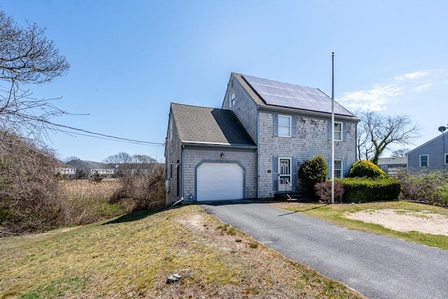view of front facade with a garage, driveway, a shingled roof, solar panels, and a front lawn