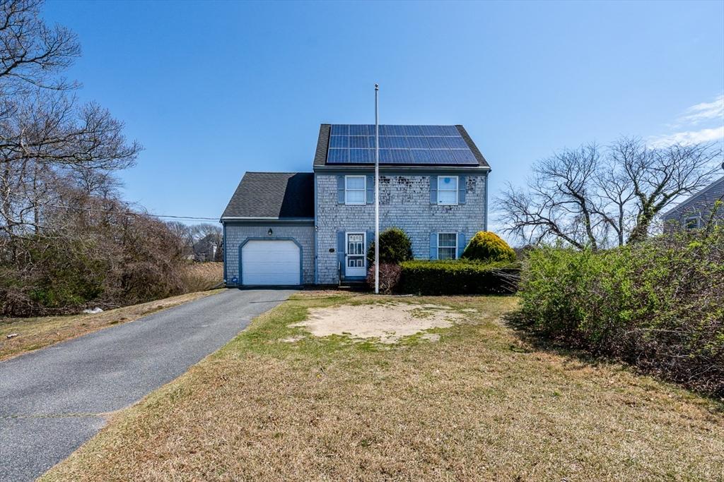 view of front of house with a garage, asphalt driveway, solar panels, and a front yard