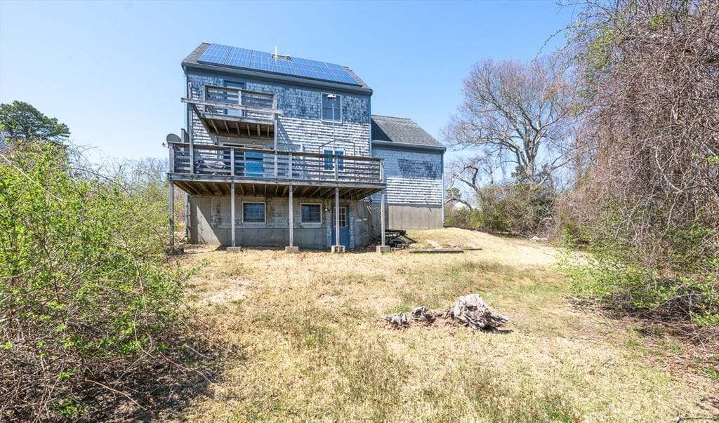 rear view of property featuring a deck and roof mounted solar panels