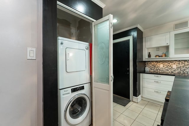 washroom featuring crown molding, stacked washer and dryer, and light tile patterned floors