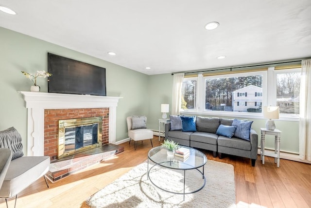 living room featuring a brick fireplace, wood-type flooring, and baseboard heating