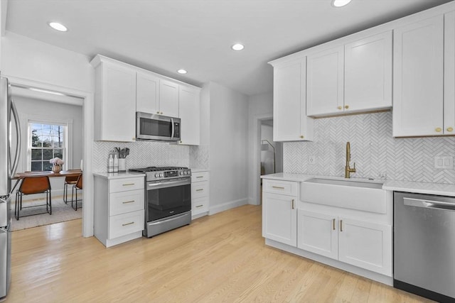 kitchen featuring stainless steel appliances, white cabinets, light countertops, and a sink