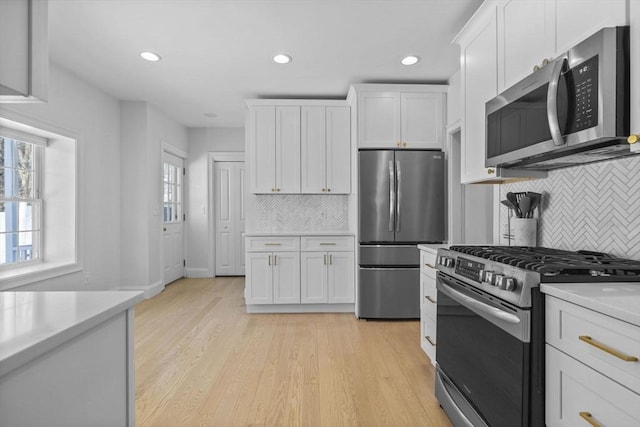 kitchen with light wood finished floors, white cabinetry, stainless steel appliances, and light countertops