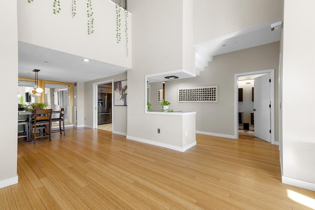 unfurnished living room with baseboards, light wood finished floors, recessed lighting, a towering ceiling, and a chandelier