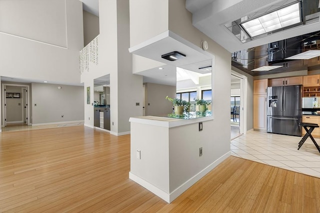 kitchen with white microwave, baseboards, stainless steel fridge with ice dispenser, a towering ceiling, and light wood-type flooring