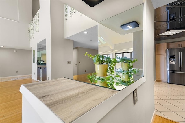 kitchen with baseboards, light wood finished floors, a high ceiling, recessed lighting, and refrigerator with ice dispenser