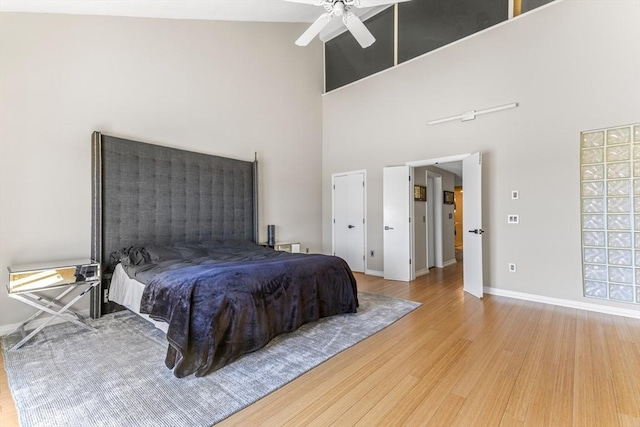 bedroom featuring ceiling fan, a high ceiling, baseboards, and wood finished floors