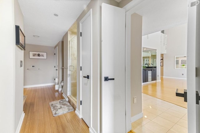 hall featuring a textured ceiling, light wood-type flooring, and baseboards