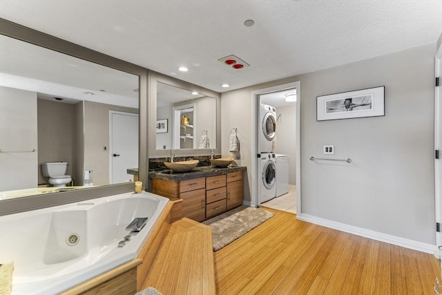 full bath featuring vanity, wood finished floors, a tub with jets, stacked washer and dryer, and toilet